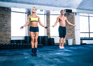 Muscular man and beautiful sporty woman workout with jumping rope in crossfit gym